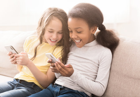 Happy little friends with smartphones sitting on sofa