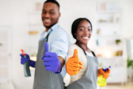 House cleaning concept. Happy black couple in rubber gloves showing thumbs up gesture at home,...
