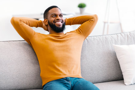 Black Guy Sitting On Couch Holding Hands Behind Head Indoorの写真素材