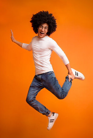 Happy black guy jumping on orange studio background