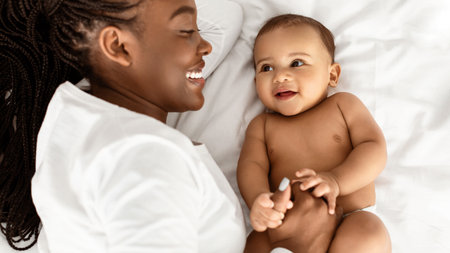 African American mom lying in bed with her cute babyの写真素材