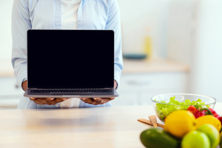 Unrecognizable Woman Showing Laptop Empty Screen Standing In Modern Kitchenの写真素材