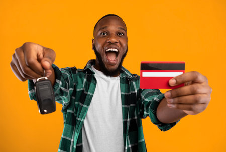 African Man Showing Car Key And Credit Card, Yellow Backgroundの写真素材