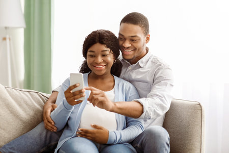 Loving black expecting parents shopping online, using smartphoneの写真素材