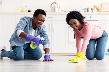 Cheerful african american couple cleaning floor together in kitchenの写真素材