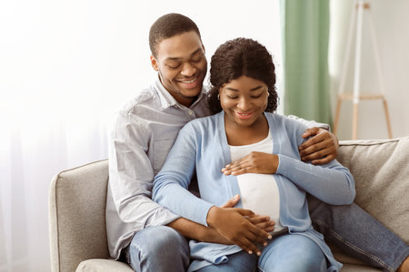 Smiling man hugging his pregnant woman, sitting on sofaの写真素材