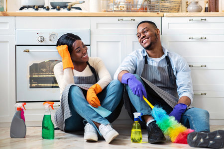 Full length of happy black couple sitting on kitchen floor after house cleanup, resting, enjoying each others companyの写真素材