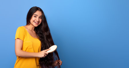 Smiling Young Indian Woman Brushing Long Hair With Wooden Combの写真素材