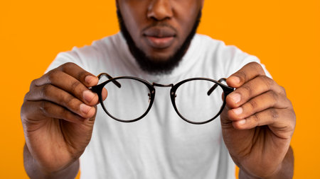 African Man Holding Glasses Having Poor Eyesight, Yellow Background, Croppedの写真素材