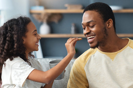 Cute curly girl feeding her daddy, drinking tea togetherの写真素材