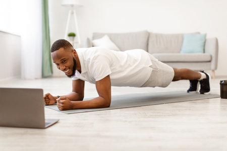 Black Man At Laptop Standing In Plank Exercising At Homeの写真素材
