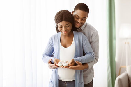 Happy pregnant african american family holding small baby bootiesの写真素材