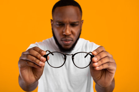 Man Holding Eyeglasses Squinting Eyes Having Poor Eyesight, Yellow Backgroundの写真素材
