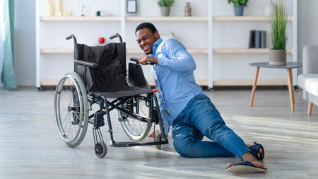 Young black man with disability lying on floor after falling down from wheelchair at homeの写真素材