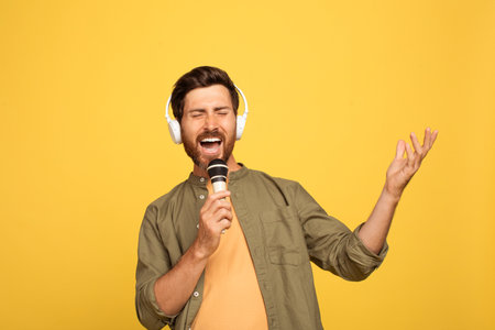 Happy middle aged man singing into a mic with a yellow backdropの写真素材