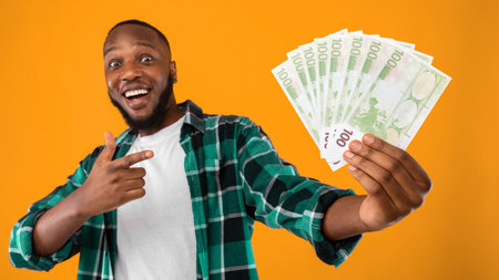 African Man Holding Money Pointing Finger At Cash, Yellow Backgroundの写真素材