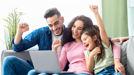 Happy arabic family of three celebrating success with laptop at homeの写真素材