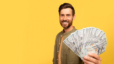 Smiling man holds cash while posing in front of a bright yellow backgroundの写真素材