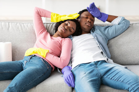 Tired african american man and woman resting after cleaning apartmentの写真素材