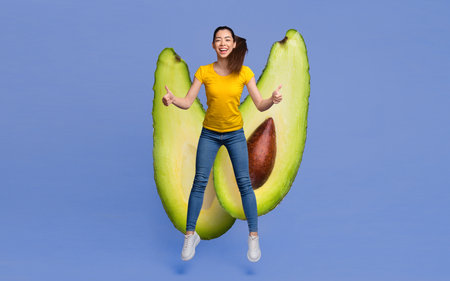 Jumping woman celebrates with avocado on vibrant blue backgroundの写真素材