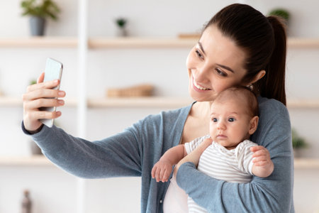 Beautiful Young Mother Taking Selfie With Her Adorable Newborn Baby At Homeの写真素材