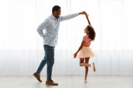 Black dad and daughter dancing at home, full length shotの写真素材