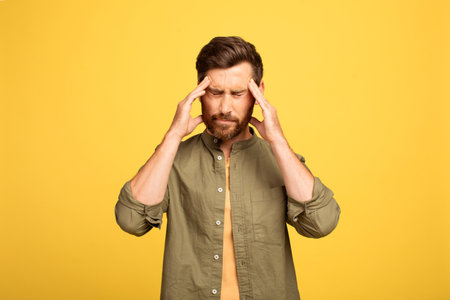 Man experiencing stress while standing against a yellow backgroundの写真素材