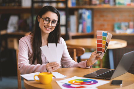 Creative latin woman web-designer working with color palette while sitting at cafe with laptop, free spaceの写真素材