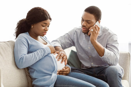 Worried black husband calling doctor while wife having labor painsの写真素材