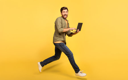 Middle aged man runs while working on his laptop in a bright yellow settingの写真素材