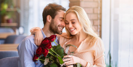 Millennial couple in love hugging and cuddling in cafe, holding bouquet of flowers, celebrating Valentines Dayの写真素材