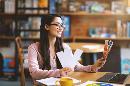 Young creative graphic designer with color sets at cafe, using laptop and drinking coffee, empty spaceの写真素材