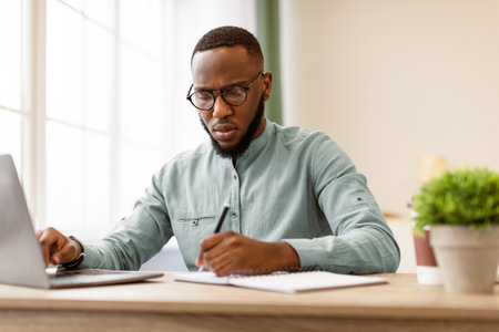 Black Businessman Taking Notes Sitting Working At Workplace In Officeの写真素材
