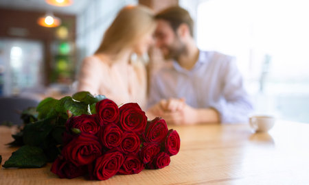 Bouquet of red roses on table at coffee shop and romantic young couple on background, selective focusの写真素材