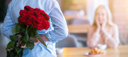 Romantic young guy with bouquet of red roses behind his back making surprise for his girlfriend at cafe, free spaceの写真素材