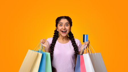 Excited indian woman holding plastic credit card and shopping bagsの写真素材