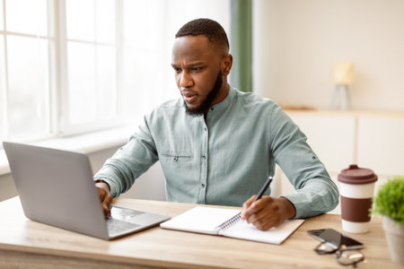 Black Businessman Working Taking Notes And Using Laptop At Workplace