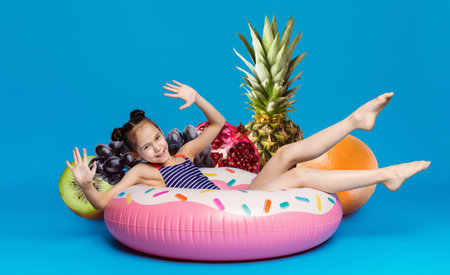 Child enjoying summer fun on a pink inflatable donut with fruit backdropの写真素材