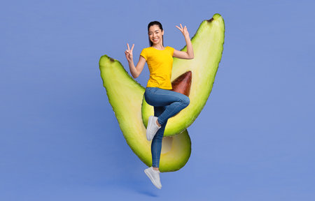 Joyful young woman poses with large avocado halves on blue backgroundの写真素材