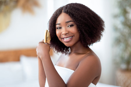 Portrait of happy young black lady brushing her curly dark hair at homeの写真素材