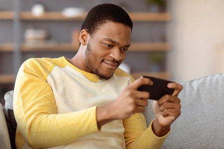 Concentrated black guy playing game on mobile phoneの写真素材