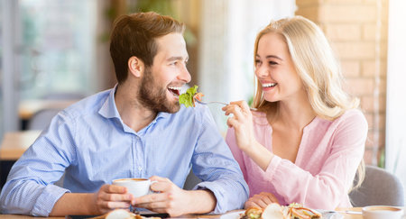 Lovely young woman feeding her boyfriend with fresh salad at coffee shopの写真素材