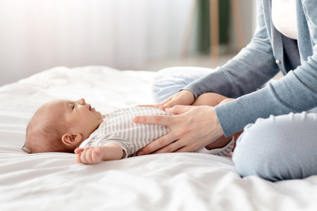 Loving Mother Making Belly Massage To Newborn Baby On Bed At Home