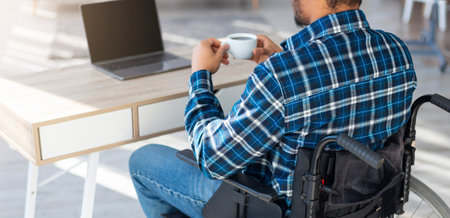 Unrecognizable black man in wheelchair using laptop for online work from home, having coffee, mockupの写真素材
