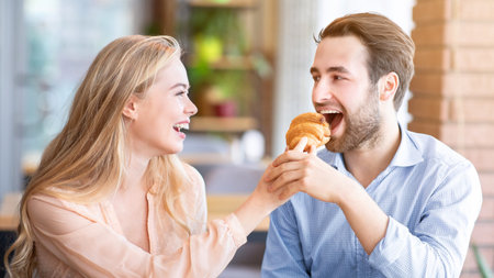 Loving young woman feeding yummy croissant to her boyfriend at urban cafeの写真素材
