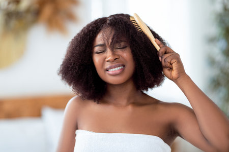 Frustrated millennial black woman trying to brush her tangled hair at home. Domestic hairdressing conceptの写真素材