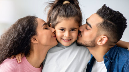 Happy Childhood. Loving Arabic Parents Kissing Their Little Daughter In Both Cheeksの写真素材
