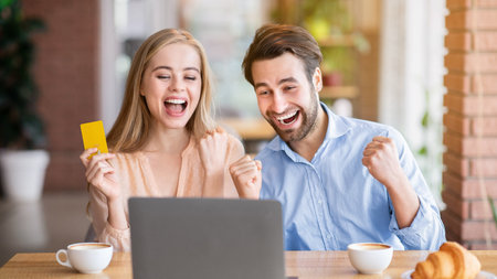 Cheerful Caucasian couple with credit card and laptop shopping online at city cafeの写真素材
