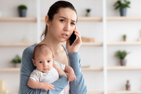 Worry Young Mother Holding Newborn Baby On hands And Talking On Cellphoneの写真素材