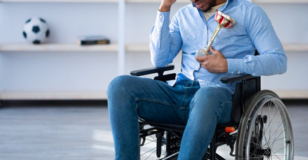 Black sportsman with trophy sitting in wheelchair, feeling depressed over his injury at home